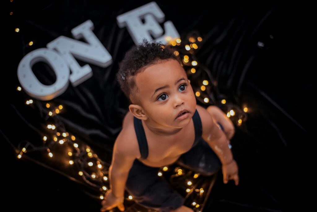 Cute toddler surrounded by warm bokeh lights and the word 'ONE' in playful background.